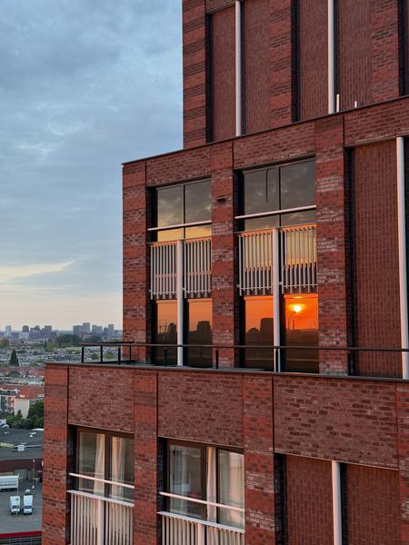 This photo captures a stunning sunset reflecting vividly in the windows of a modern brick building at Jan van Galenstraat, West, Amsterdam